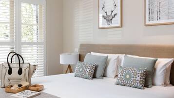 Un dormitorio con cama, almohadas, un bolso de mano, una lámpara y un cuadro en la pared.