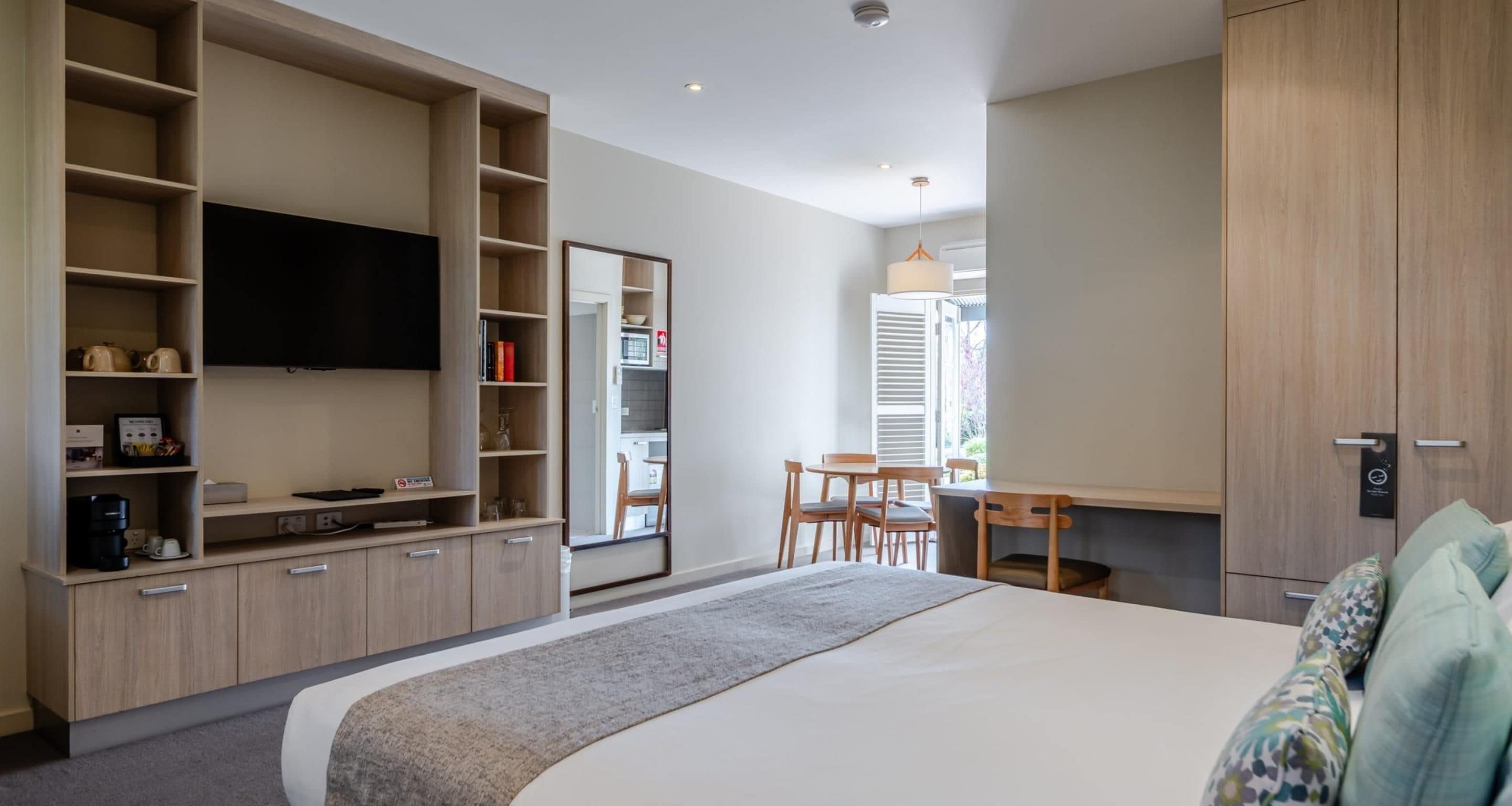 Un dormitorio moderno con una cama grande, estanterías empotradas, un televisor de pantalla plana, un escritorio con sillas y un armario.