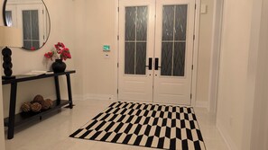 A hallway with a black and white checkered rug, a console table with a vase of flowers, and a double door with frosted glass panels. - Minutes to Ski ,Golf & Spa | Private Retreat (Oro-Medonte)