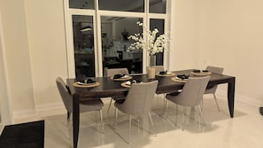A dining table with six chairs, a vase with flowers, and a kitchen visible through a glass door. - Minutes to Ski ,Golf & Spa | Private Retreat (Oro-Medonte)