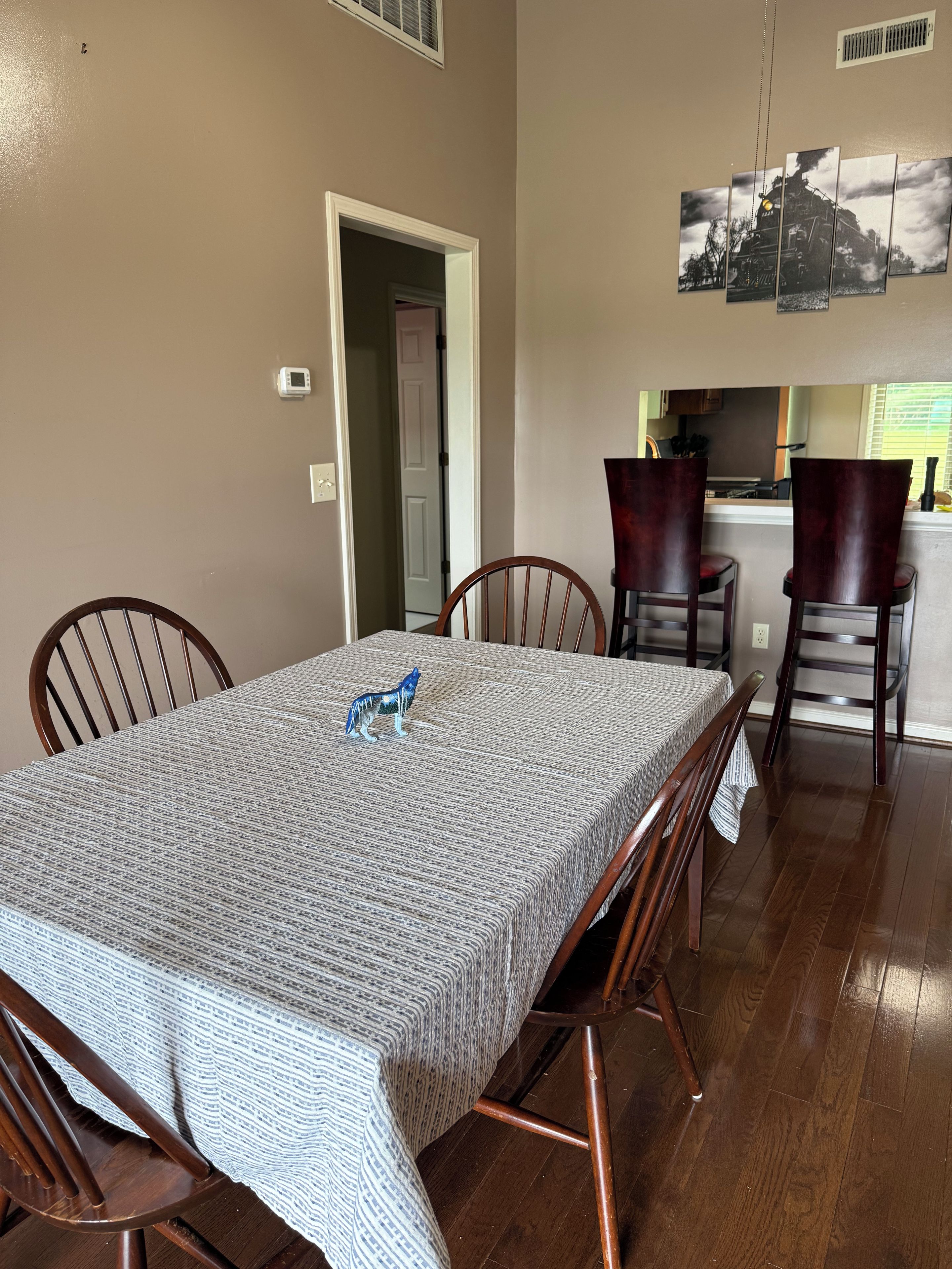 A dining area with a table set for four, wooden chairs, and a kitchen visible in the background.