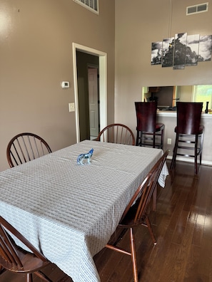 A dining area with a table set for four, wooden chairs, and a kitchen visible in the background.
