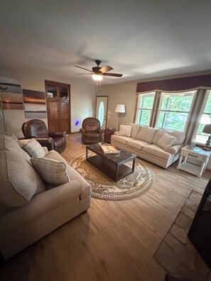 A living room with a brown leather chair, a beige sofa, a coffee table, and a ceiling fan. - Stillwater Cove - Pontoon included + Golf (Mount Gilead)