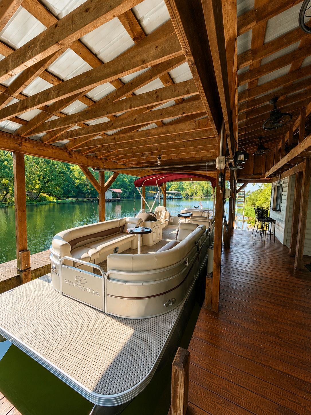 Un muelle cubierto con zona de estar, vigas de madera y vista al lago.