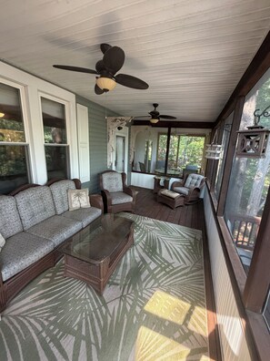 Eine überdachte Veranda mit Korbmöbeln, Deckenventilatoren und großen Fenstern.
