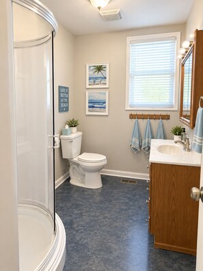 A bathroom with a glass shower enclosure, a toilet, a sink, and a vanity with a mirror. There are two framed pictures on the wall and a window with blinds. - Stillwater Cove - Pontoon included + Golf (Mount Gilead)