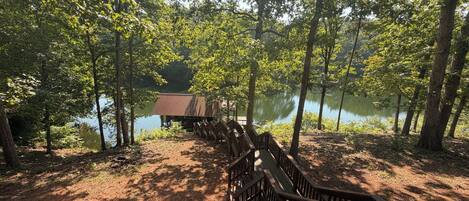 A wooden deck leading to a rustic cabin by a lake surrounded by trees.