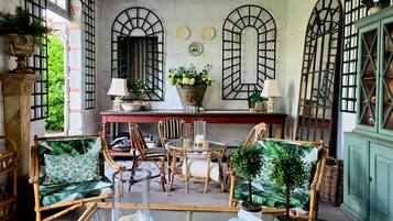 A room with a dining table, chairs, a sofa, and a window with a view of greenery.