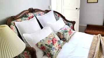 A neatly made bed with floral-patterned pillows and a white bedspread, a bedside table with a lamp, and a door with a mirror above it.