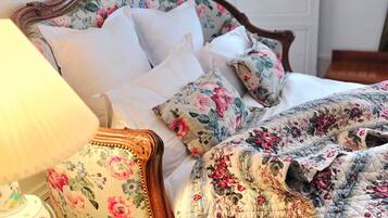 A bed with a floral headboard, a bedside table with a lamp, and a door in the background.
