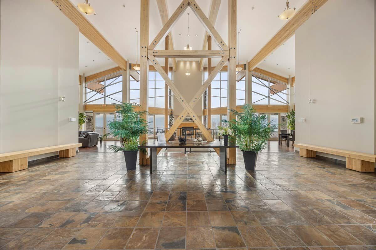 Un hall d’entrée spacieux avec un plafond haut, des poutres en bois et un espace salon central.