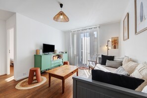 Una sala de estar moderna con una televisión, un aparador verde, una mesa de madera, un sofá y una lámpara de pie.