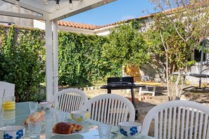 An outdoor dining area with a table set for two, chairs, and a grill. - Holiday Home 'Porteau rouge' gîte de la Presqu'île (L'Aiguillon-la-Presqu'île)
