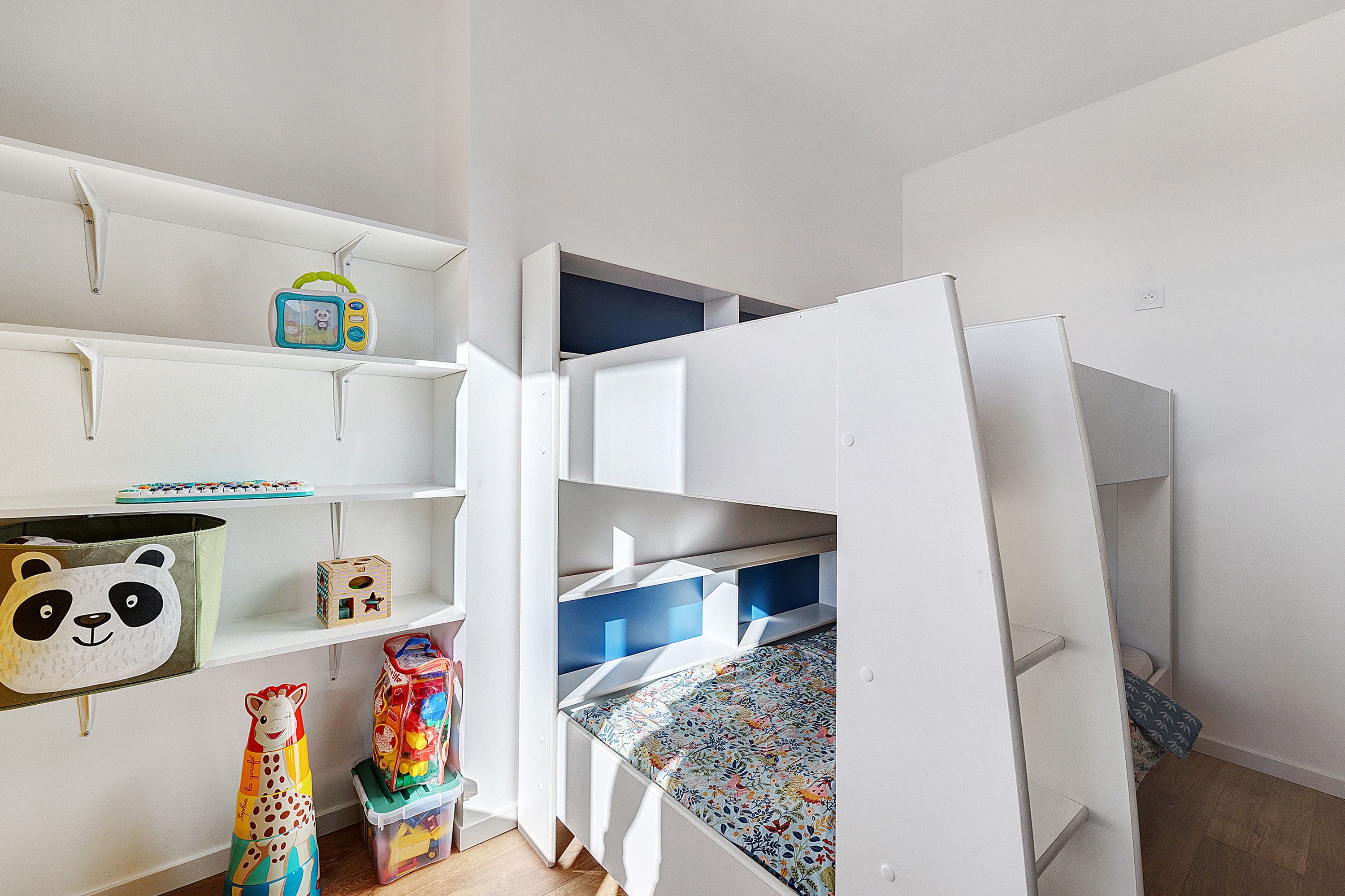 Une chambre d’enfant avec un lit superposé, des étagères remplies de jouets et une boîte de rangement décorée sur le thème des pandas.