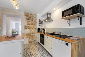 Una cocina con pared de piedra, encimera de madera, horno empotrado y microondas.