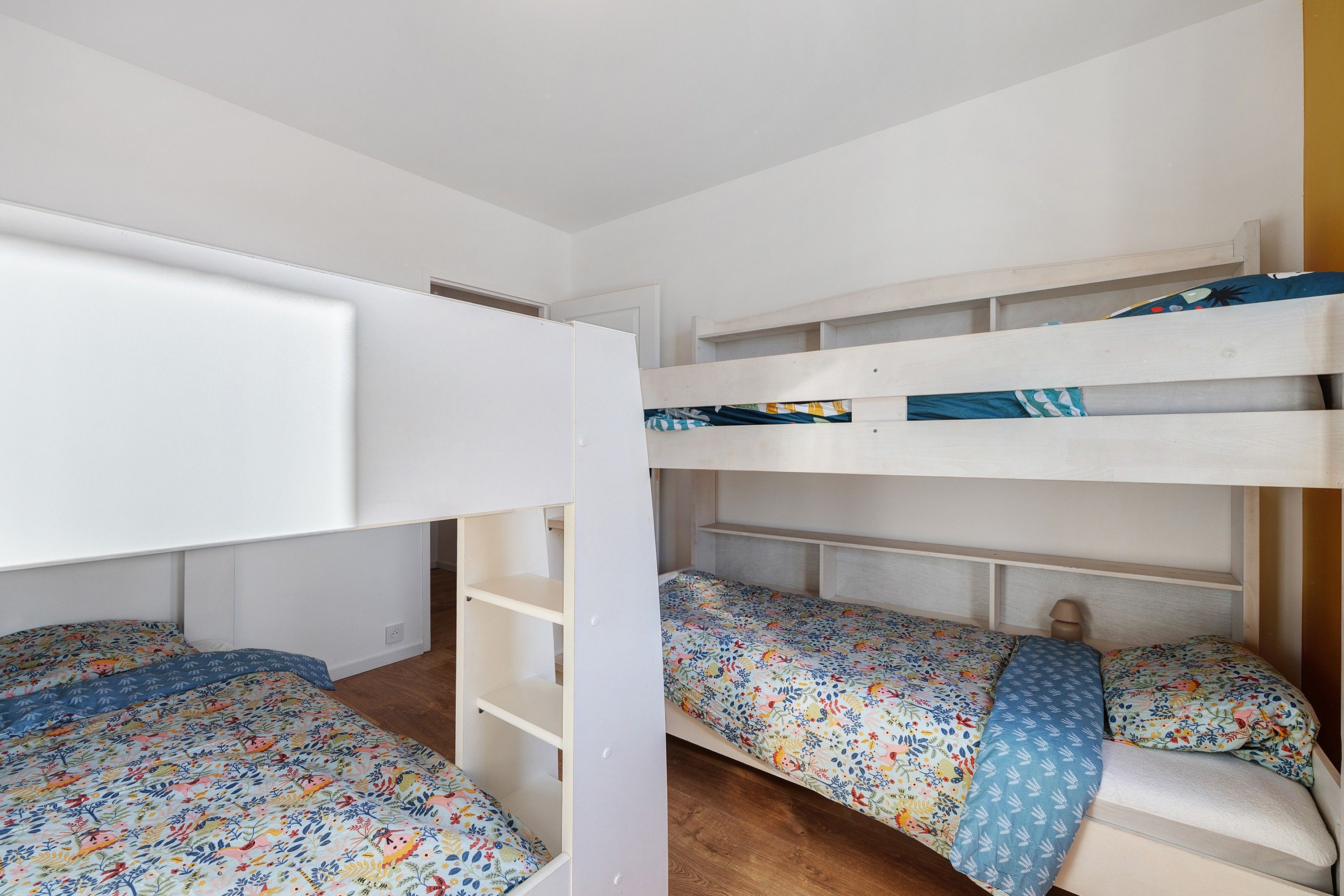 Une chambre avec un lit superposé, un plafond blanc et un plancher en bois.