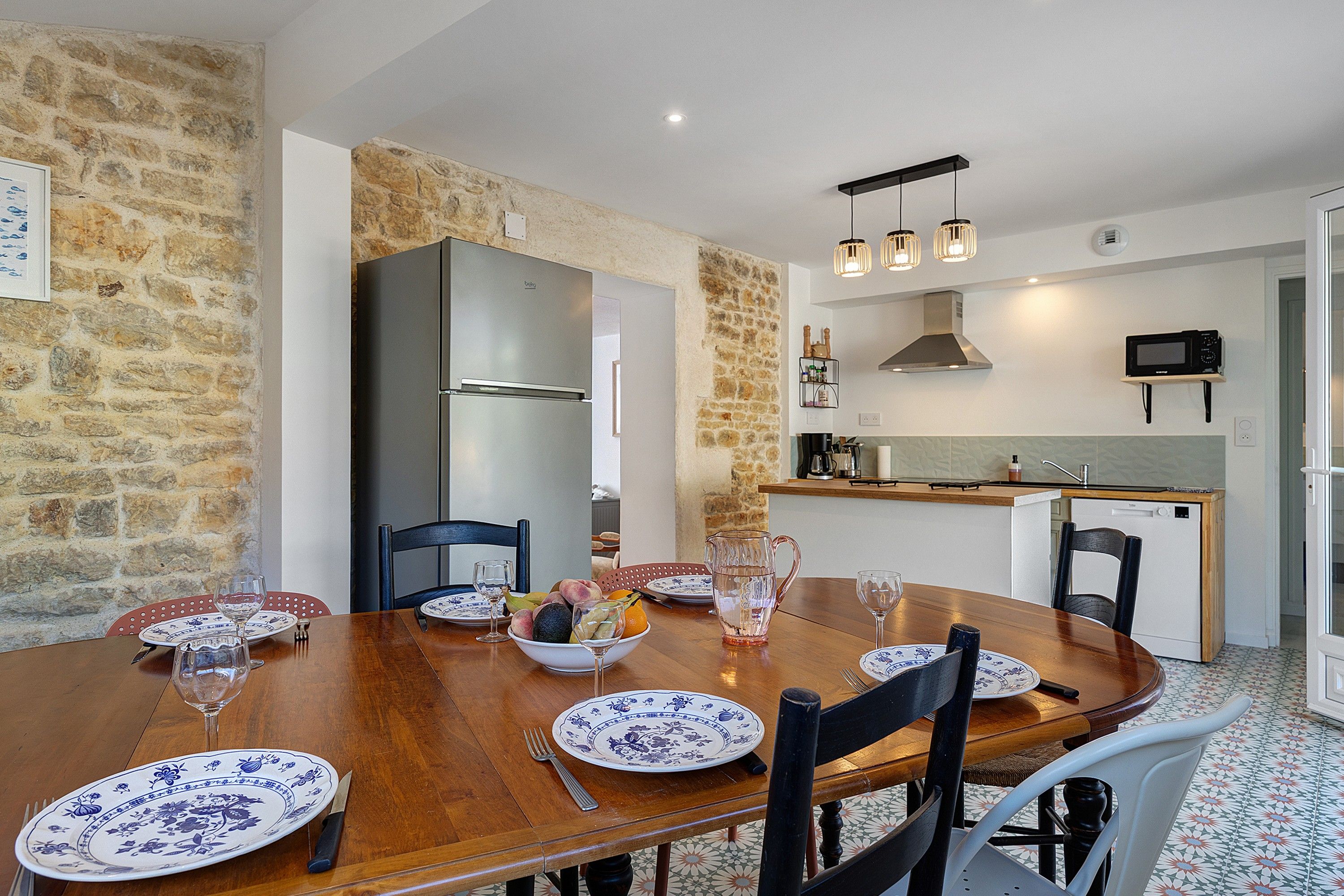 Un coin repas avec une table en bois, dressée pour quatre personnes et entourée de chaises, ainsi qu’une cuisine équipée d’appareils électroménagers modernes.