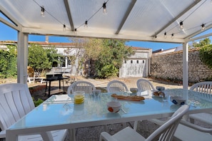 An outdoor patio with a glass table, white chairs, and string lights. - Holiday Home 'Porteau rouge' gîte de la Presqu'île (L'Aiguillon-la-Presqu'île)
