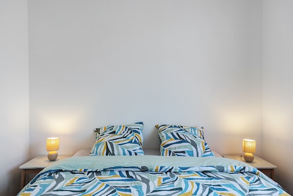 Una cama con una colcha estampada y dos almohadas, flanqueada por dos mesitas de noche con lámparas.
