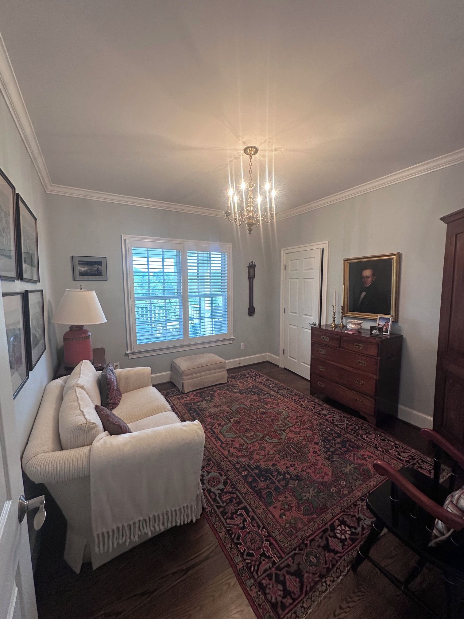 A room with a white sofa, a patterned rug, a wooden dresser, and a chandelier.