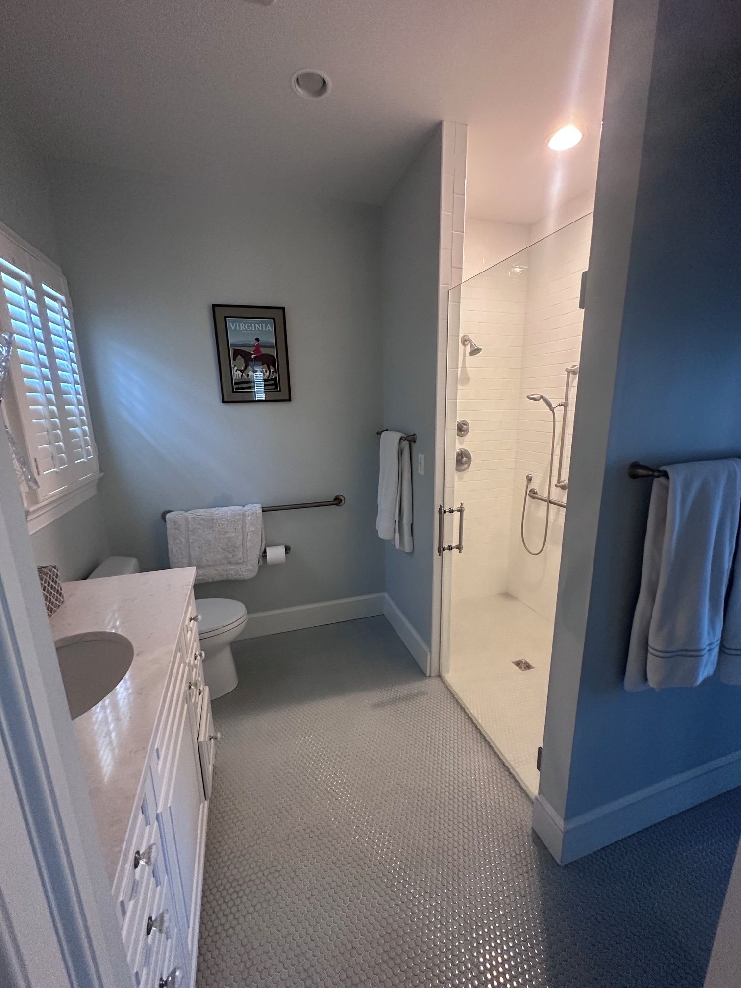 A bathroom with a toilet, sink, shower, and a framed picture on the wall.