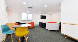 A conference room with a round table, colorful chairs, a whiteboard, and a window with a view of buildings. - Student Only Miura (Nottingham)