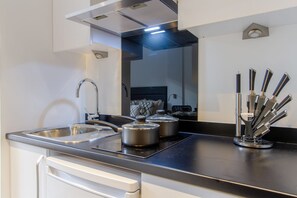 A modern kitchen with stainless steel appliances, a sink, and a range hood. - Student Only Miura (Nottingham)