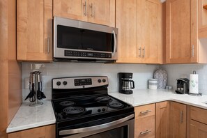 A kitchen with wooden cabinets, a stainless steel microwave, a black stove, and a coffee maker. - Bradley Creek Retreat 5 min to Wrightsville Beach (Wilmington)