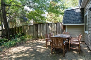 An outdoor patio area with a table and chairs, surrounded by a wooden fence and trees. - Bradley Creek Retreat 5 min to Wrightsville Beach (Wilmington)