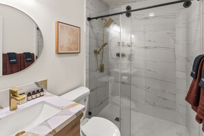 Un baño moderno con ducha envuelta en vidrio, tocador de mármol y un espejo grande.