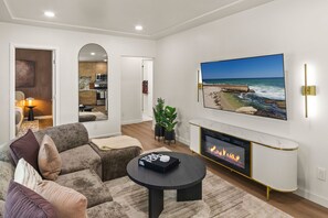Una sala de estar moderna con chimenea, un televisor grande montado en la pared y vistas a la playa a través de la ventana.