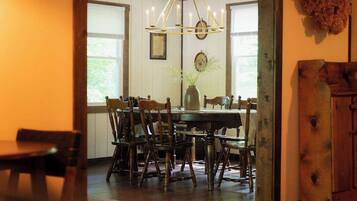 A dining area with a wooden table and chairs, a chandelier, and a vase with greenery.