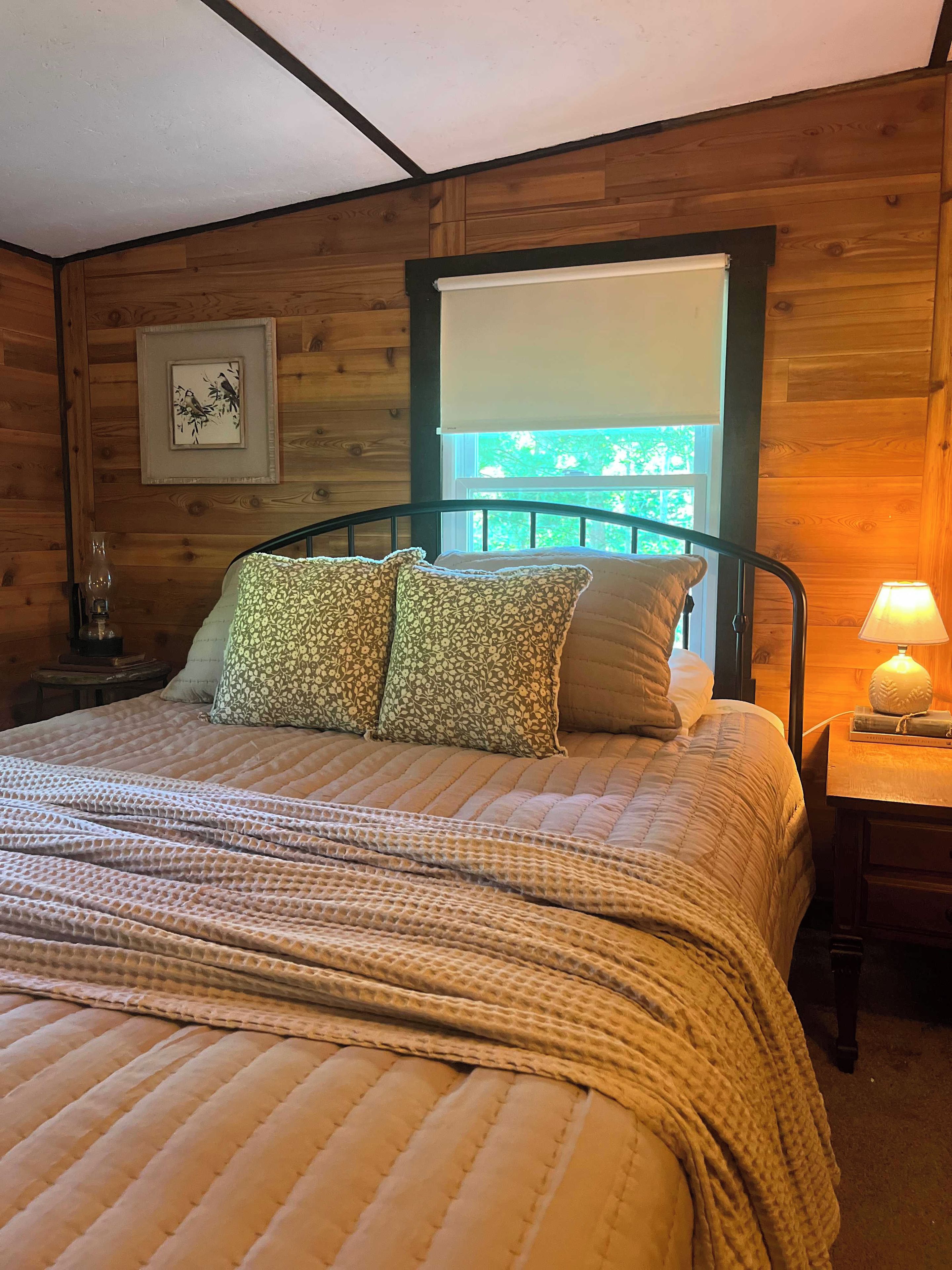 A wooden-paneled room with a bed, pillows, a nightstand, a lamp, and a window.