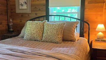 A wooden-paneled room with a bed, pillows, a nightstand, a lamp, and a window.