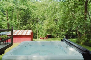 A hot tub in a wooded backyard with a red shed and a wooden deck. - Charming Creekside Villa With Hot tub (Laurelville)