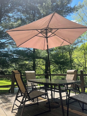 A wooden deck with a table and chairs, an umbrella, and a view of trees. - Charming Creekside Villa With Hot tub (Laurelville)