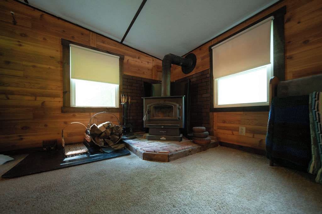 A cozy cabin interior with a wood-burning stove, large windows, and a log fire.