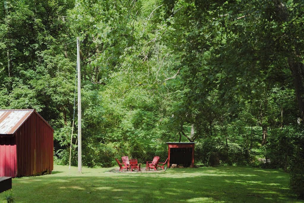 A red building with a metal roof, surrounded by a grassy area with red chairs and a small shed.