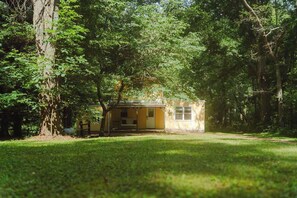 A small, single-story building surrounded by dense trees. - Charming Creekside Villa With Hot tub (Laurelville)
