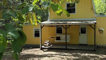 Une maison jaune avec un porche, un banc et une petite table.