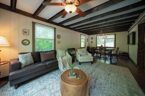 A living room with a sofa, armchairs, a dining table with chairs, a wooden coffee table, and a ceiling fan.