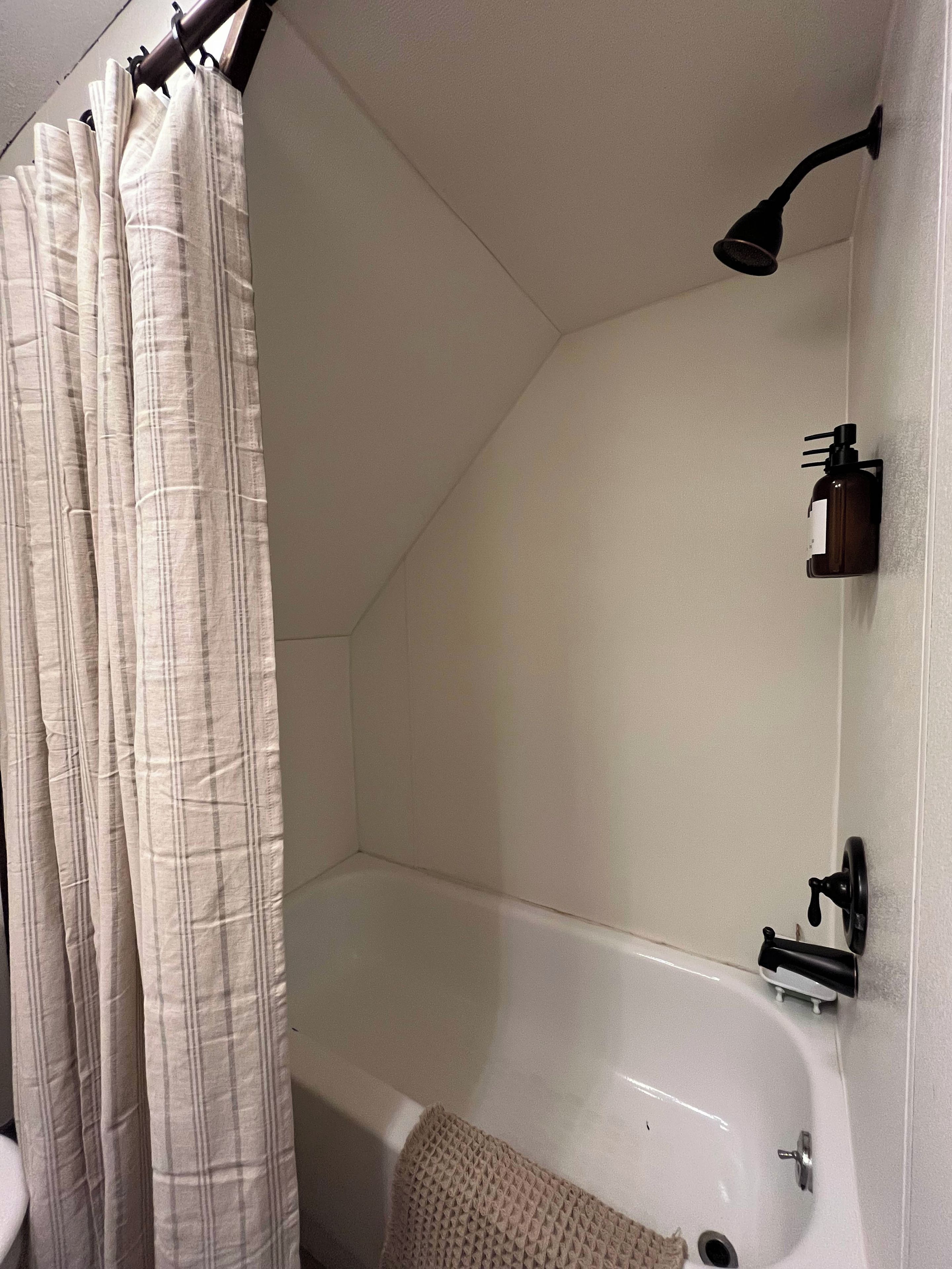 A bathroom with a bathtub, a shower curtain, a handheld showerhead, and a bottle of shampoo on the wall.