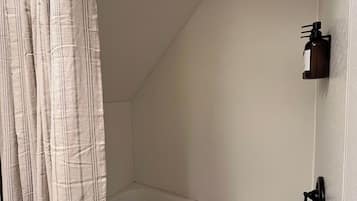 A bathroom with a bathtub, a shower curtain, a handheld showerhead, and a bottle of shampoo on the wall.