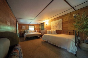 A cozy room with two beds, a chair, and a large window. - Charming Creekside Villa With Hot tub (Laurelville)
