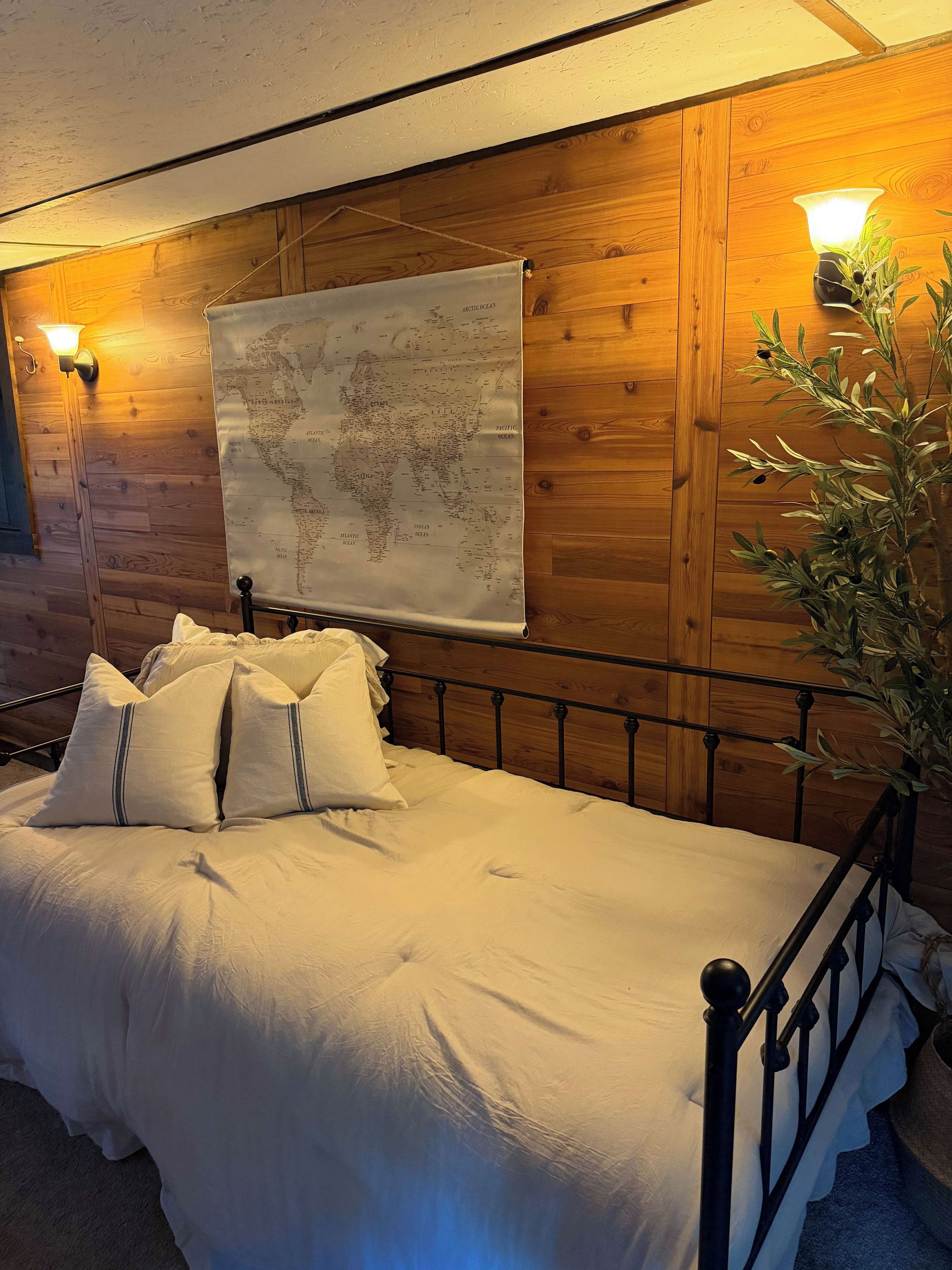 A bed with white bedding and pillows, a wooden wall, a map, and a wall-mounted lamp.