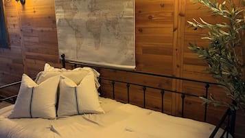 A bed with white bedding and pillows, a wooden wall, a map, and a wall-mounted lamp.