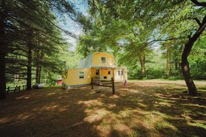 A yellow cabin with a fenced yard, surrounded by trees.