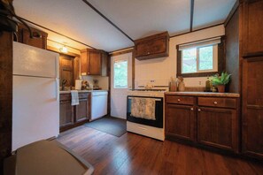 A compact kitchen with wooden cabinets, a white refrigerator, a stove, and a window.