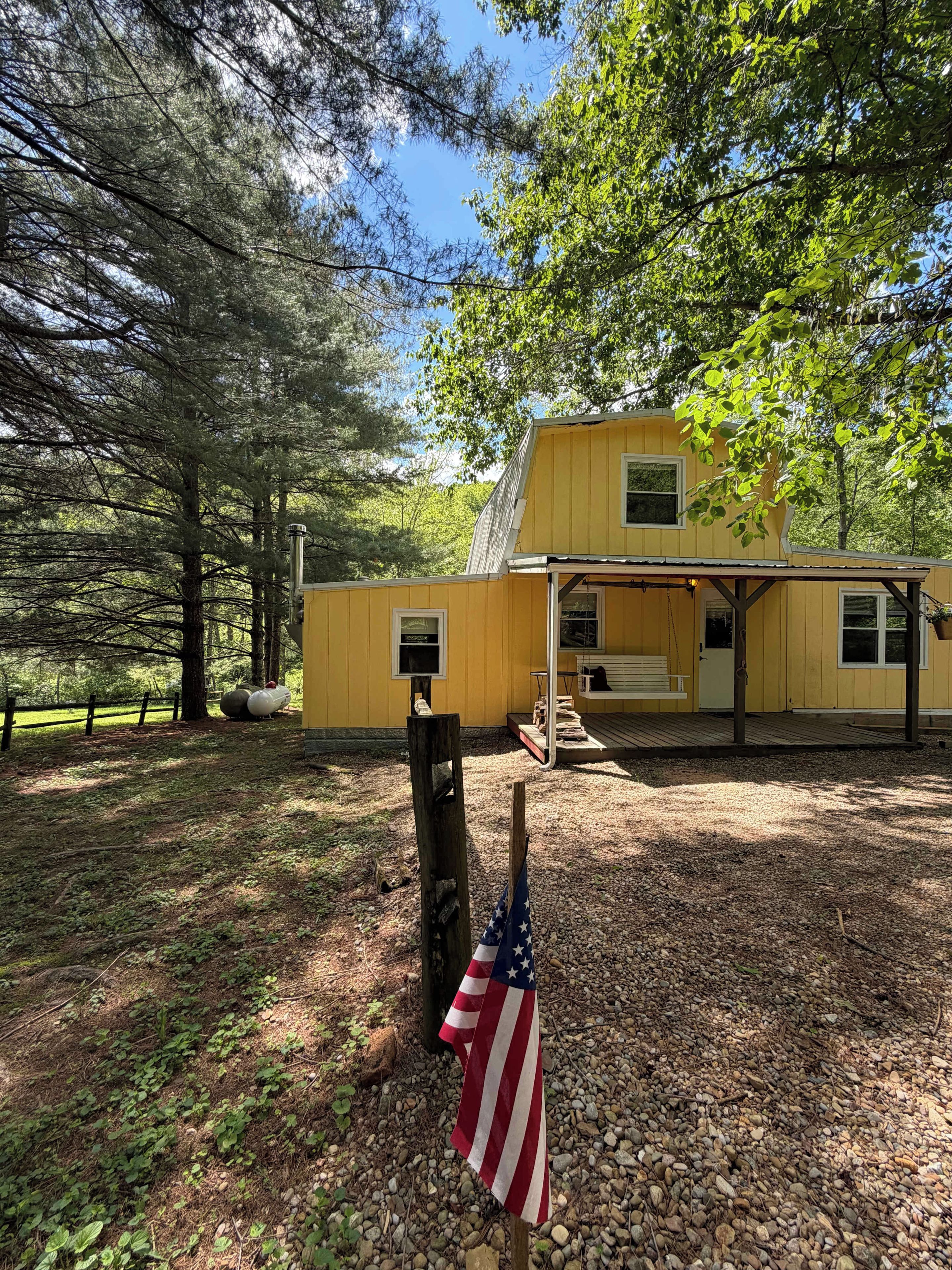 A yellow cabin with a porch, surrounded by trees and gravel ground.