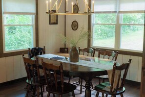 A dining room with a wooden table, chairs, a vase with branches, and a chandelier.